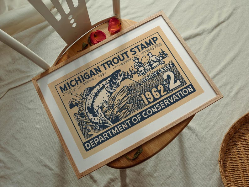 May include: Framed vintage print of a Michigan Trout Stamp from 1962. The artwork features a leaping trout, fishermen, and the text "Department of Conservation." The print is in a light wood frame.