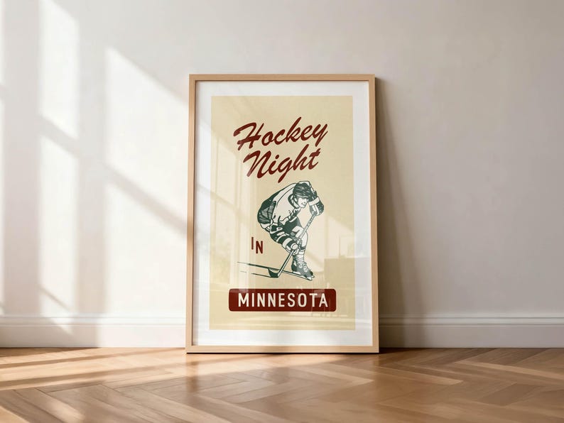 Puede incluir: P&oacute;ster enmarcado de estilo vintage con una ilustraci&oacute;n de un jugador de hockey. El p&oacute;ster presenta el texto "Hockey Night" en una escritura burdeos encima del jugador, con "IN" y "MINNESOTA" debajo. El fondo es de color crema.