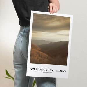 Op de afbeelding: Een poster met een foto van een bergketen met een bewolkte lucht. De tekst "GREAT SMOKY MOUNTAINS NATIONAL PARK" staat onderaan de poster.