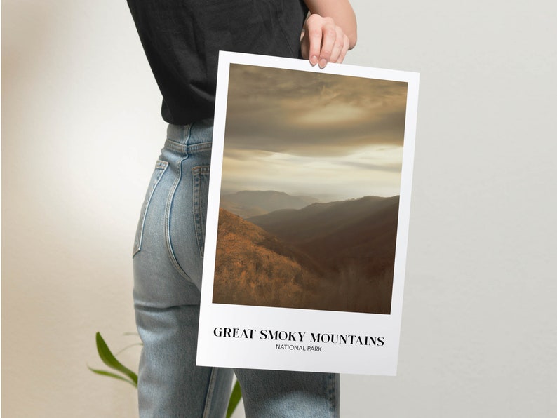 Op de afbeelding: Een poster met een foto van een bergketen met een bewolkte lucht. De tekst "GREAT SMOKY MOUNTAINS NATIONAL PARK" staat onderaan de poster.