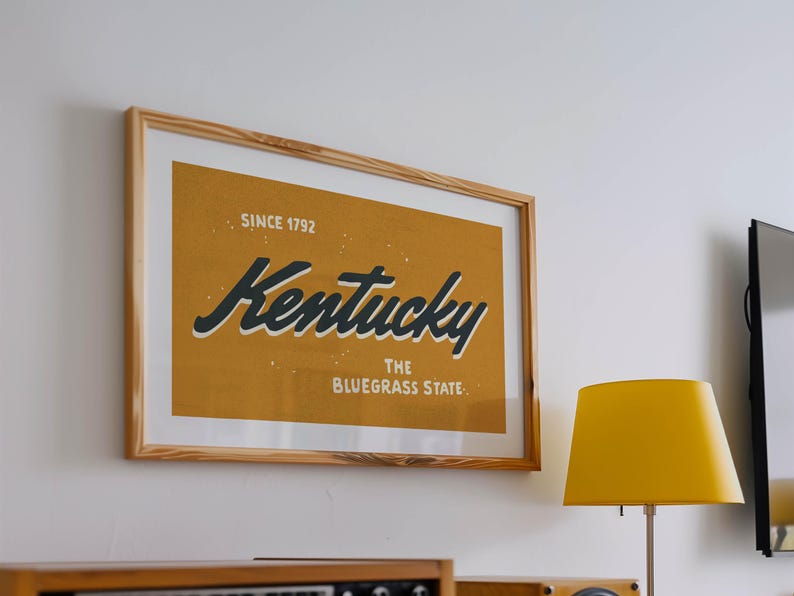 May include: A framed print with a yellow background and black text that reads "Kentucky, The Bluegrass State, Since 1792".