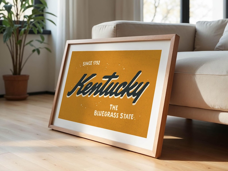 May include: A framed print with a yellow background and black text that reads "Kentucky, The Bluegrass State, Since 1792".