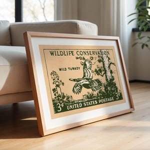 May include: Framed vintage print with a green illustration of a wild turkey in flight on a tan background. Text reads "Wildlife Conservation" and "United States Postage 3&cent;". The print is in a light wood frame.