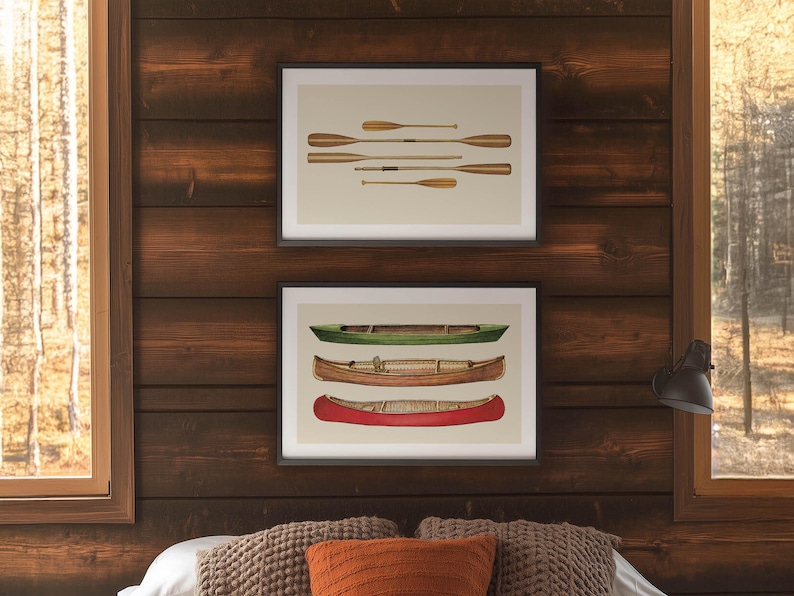 May include: Two framed prints on a wood-paneled wall. The top print features a collection of wooden oars. The bottom print showcases three canoes in green, brown, and red. The artwork is displayed above a bed with decorative pillows.
