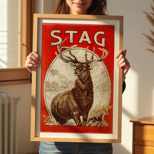 May include: A framed vintage poster with a red background and the word "STAG" in large, bold letters. A detailed illustration of a stag with large antlers stands in a forest setting.