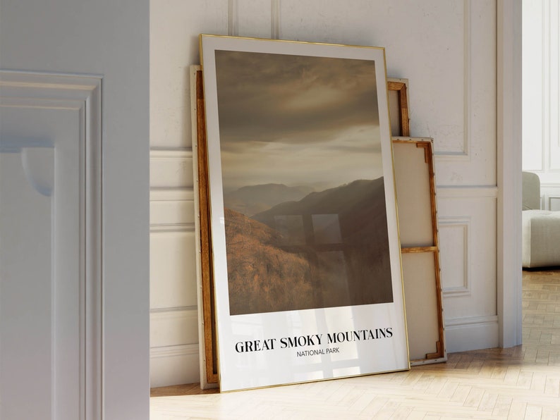 Op de afbeelding: Een ingelijste print met een foto van een bergketen met een bewolkte lucht. De print heeft een gouden lijst en de tekst "GREAT SMOKY MOUNTAINS NATIONAL PARK" onderaan.