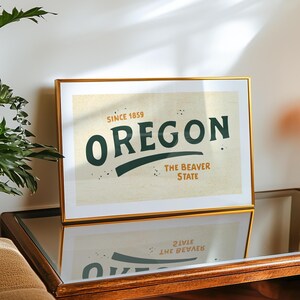 May include: A gold framed print with a vintage design featuring the text "Oregon, Since 1859, The Beaver State" in green and black lettering on a cream background.