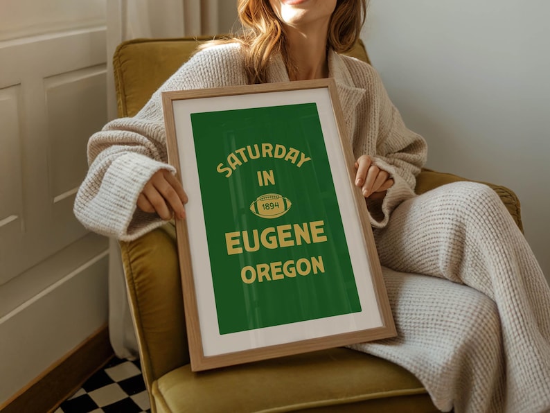 K&ouml;nnte beinhalten: Gerahmtes Poster mit gr&uuml;nem Hintergrund und goldenem Text "Saturday in Eugene Oregon 1894". Das Poster zeigt eine Football-Grafik. Der Rahmen ist hellbraun.