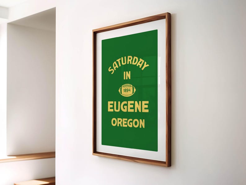 K&ouml;nnte beinhalten: Gerahmtes Poster mit gr&uuml;nem Hintergrund und goldenem Text. Der Text lautet "SATURDAY IN 1894 EUGENE OREGON" mit einer Football-Grafik. Der Rahmen hat eine dunkelbraune Holzfarbe.