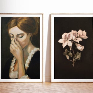 Op de afbeelding: Twee ingelijste kunstprints, een met een vrouw die haar gezicht bedekt met haar hand, en de andere met een tros delicate witte bloemen tegen een donkere achtergrond.
