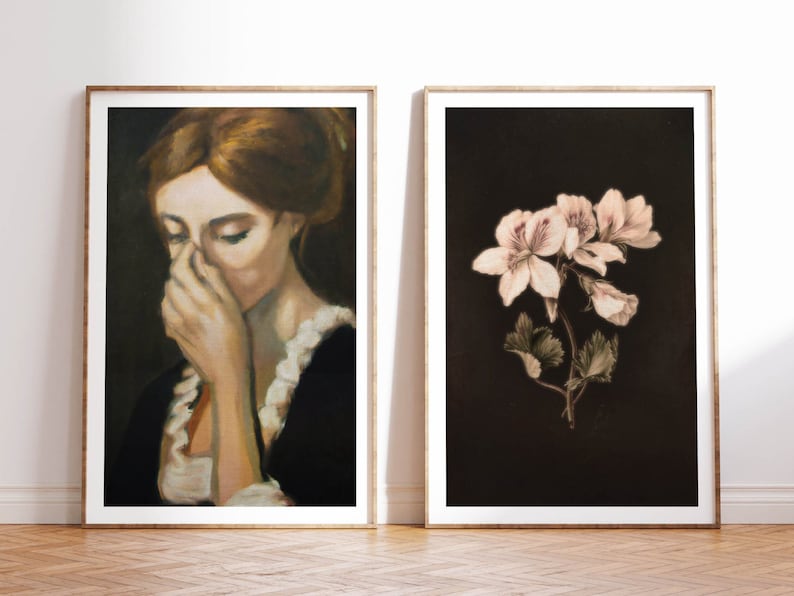 Op de afbeelding: Twee ingelijste kunstprints, een met een vrouw die haar gezicht bedekt met haar hand, en de andere met een tros delicate witte bloemen tegen een donkere achtergrond.