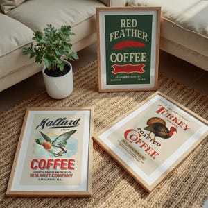 May include: Three framed vintage coffee advertisements. One features a mallard duck, another a turkey, and the third, a red feather. The frames are light wood, and the posters have a retro design with text and illustrations.