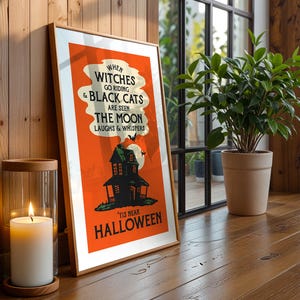 May include: A framed Halloween poster with an orange background and the text "When witches go riding & black cats are seen the moon laughs & whispers 'tis near Halloween." A lit candle sits nearby.