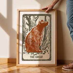 Op de afbeelding: Een ingelijste print van een bruine beer die in een bossetting zit. De print heeft een vintage stijl en de tekst "THE GREAT" staat onderaan.