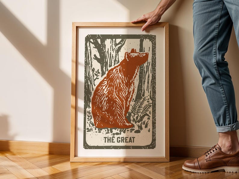 Op de afbeelding: Een ingelijste print van een bruine beer die in een bossetting zit. De print heeft een vintage stijl en de tekst "THE GREAT" staat onderaan.