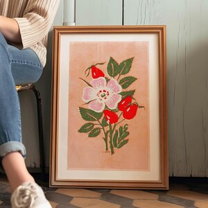 May include: A framed print of a pink and white flower with red berries and green leaves on a light pink background.