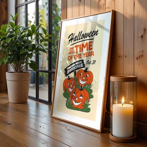 May include: Framed Halloween poster with a vintage design. The poster features orange jack-o'-lanterns and the text "Halloween, the best time of the year." A lit candle in a glass holder and a potted plant are also visible.