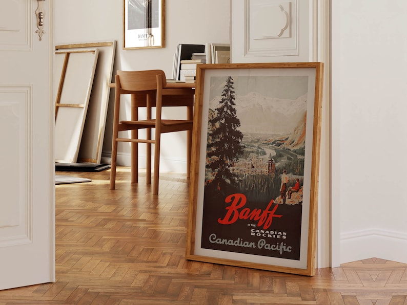 May include: A vintage travel poster in a wooden frame, advertising Banff in the Canadian Rockies with the text "Banff in the Canadian Rockies Canadian Pacific". The poster features a mountain landscape with a river and a town in the distance.