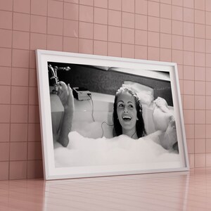 Peut inclure: Photographie en noir et blanc d'une femme dans une baignoire avec des bulles. Elle sourit et a les cheveux relev&eacute;s. La photo est encadr&eacute;e dans un cadre blanc.