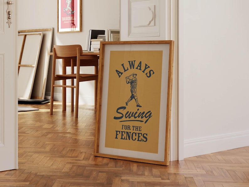 May include: A framed baseball-themed print with the text "ALWAYS Swing for the FENCES" in navy blue on a tan background. The image features a baseball player in action. The frame is a light brown color.