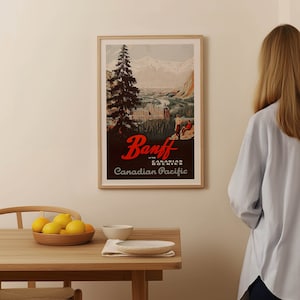 May include: A vintage travel poster advertising Banff in the Canadian Rockies. The poster features a scenic view of the mountains and a town with a large hotel. The text on the poster reads "Banff in the Canadian Rockies, Canadian Pacific."