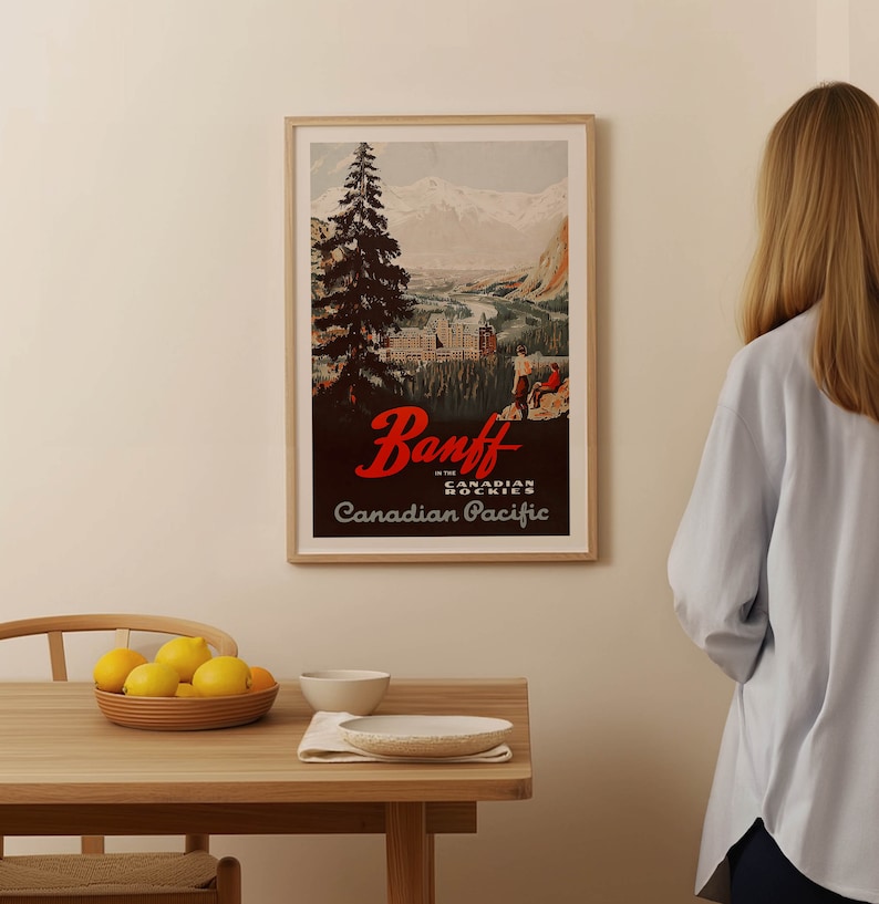 May include: A vintage travel poster advertising Banff in the Canadian Rockies. The poster features a scenic view of the mountains and a town with a large hotel. The text on the poster reads "Banff in the Canadian Rockies, Canadian Pacific."