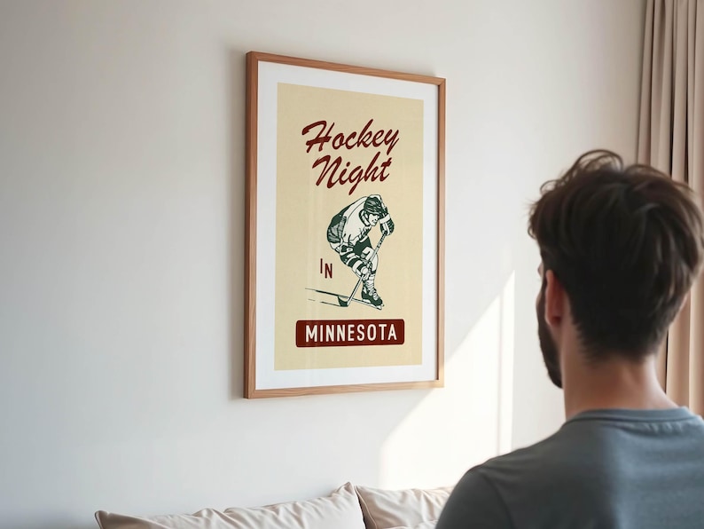 Puede incluir: P&oacute;ster enmarcado con un dise&ntilde;o vintage. El p&oacute;ster presenta las palabras "Hockey Night" en una fuente de escritura sobre una ilustraci&oacute;n de un jugador de hockey. Debajo de la ilustraci&oacute;n, el texto "IN MINNESOTA" se muestra en un recuadro.