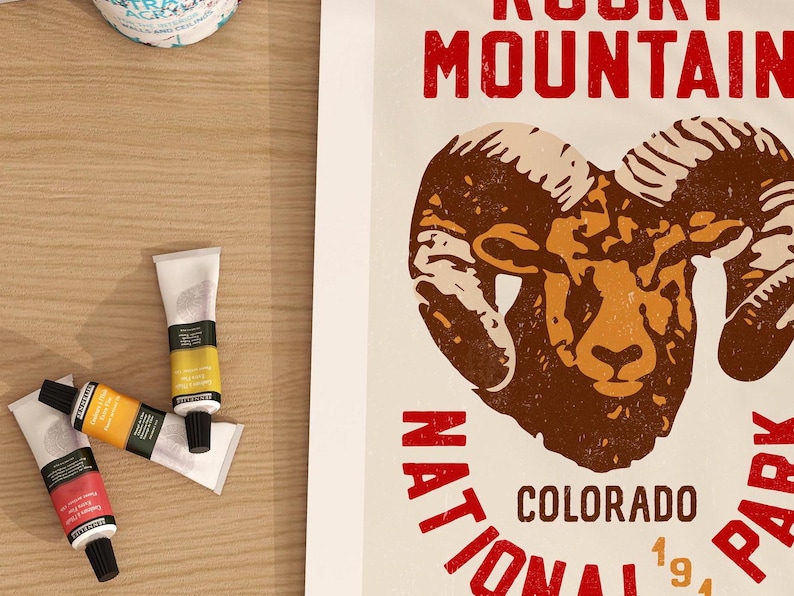 Pu&ograve; includere: Un poster in stile vintage con un ariete marrone e beige con grandi corna. Il testo "Rocky Mountain National Park Colorado 1991" &egrave; stampato in rosso e bianco.
