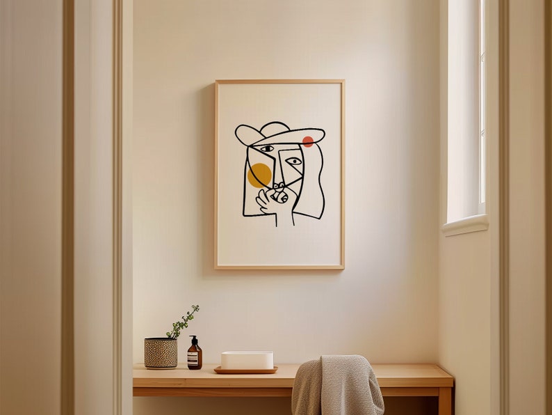 May include: A framed black and white line drawing of a face with a yellow and red circle inside. The drawing is on a white background and is framed in a light wood frame.