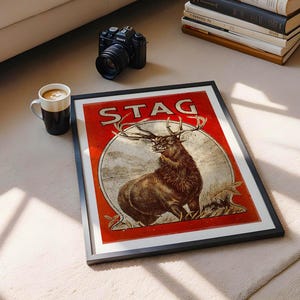 May include: A vintage-style poster with a red background and the word "STAG" in large, white letters. A brown stag with large antlers is featured in the center of the poster, standing in a forest setting.