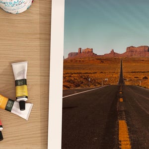 May include: A photograph of a long, straight road leading to a mountain range in the distance. The road is paved and has a yellow line down the center. The mountains are brown and rocky, and the sky is blue.