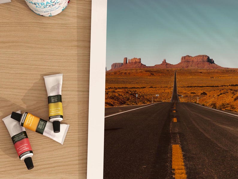 May include: A photograph of a long, straight road leading to a mountain range in the distance. The road is paved and has a yellow line down the center. The mountains are brown and rocky, and the sky is blue.