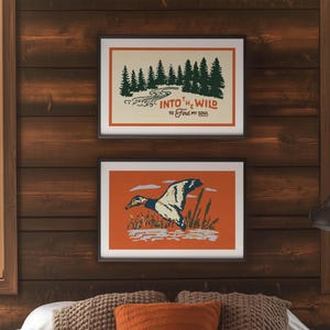 May include: Two framed art prints with nature themes hang on a wood-paneled wall. The top print features a forest scene with the text "Into the Wild to Find My Soul." The bottom print shows a duck in flight.