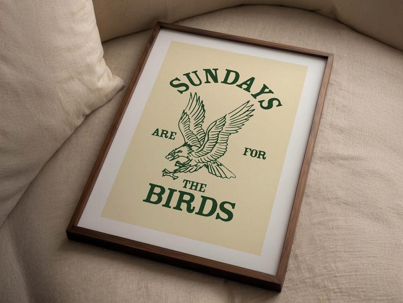 May include: Framed art print with a cream background and a green eagle illustration. The text "SUNDAYS ARE FOR THE BIRDS" is printed above and below the eagle. The frame is dark brown.