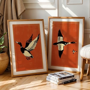 May include: Two framed prints of stylized black and white ducks on a burnt orange background. The ducks are flying in different directions.