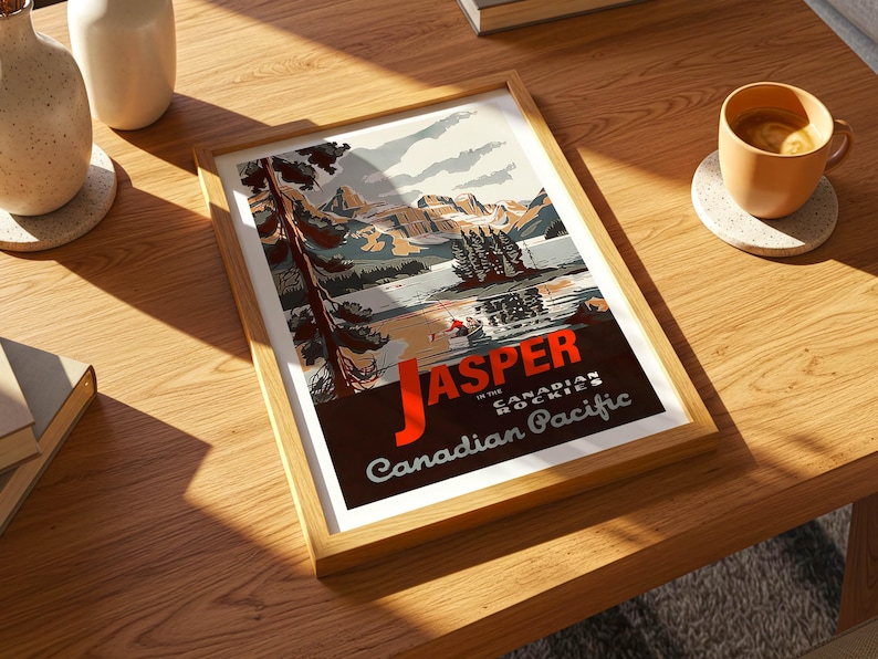 Op de afbeelding: Een ingelijste kunstafdruk met een vintage reisaffiche voor Jasper in de Canadese Rockies. De poster toont een landschap met bergen, een meer en de tekst "Jasper in the Canadian Pacific". De lijst is van licht hout.