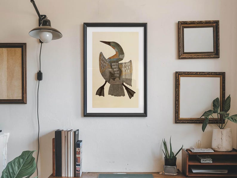 May include: A framed print of a bird with outstretched wings, featuring shades of brown, gray, and beige. The artwork is displayed on a cream-colored wall, alongside two smaller framed mirrors and a wooden shelf with plants and books.