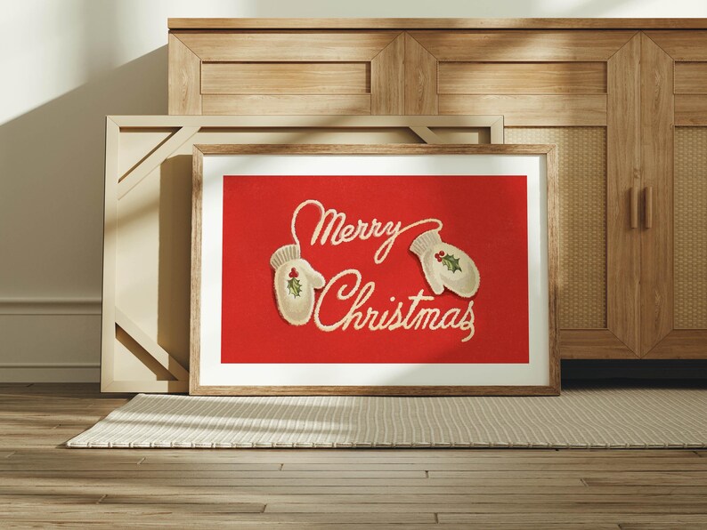 May include: Framed art print with a red background and the words "Merry Christmas" in cursive script. Two white mittens with holly accents are on the red background. The art is in a wooden frame.