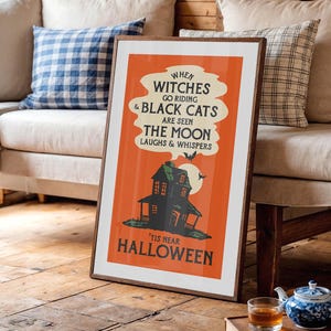 May include: Framed Halloween-themed poster with a vintage design. The orange poster features a haunted house illustration, bats, and the text "When witches go riding & black cats are seen the moon laughs & whispers 'tis near Halloween."