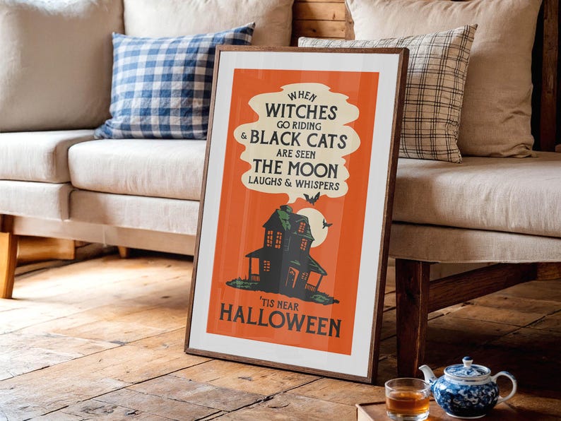 May include: Framed Halloween-themed poster with a vintage design. The orange poster features a haunted house illustration, bats, and the text "When witches go riding & black cats are seen the moon laughs & whispers 'tis near Halloween."