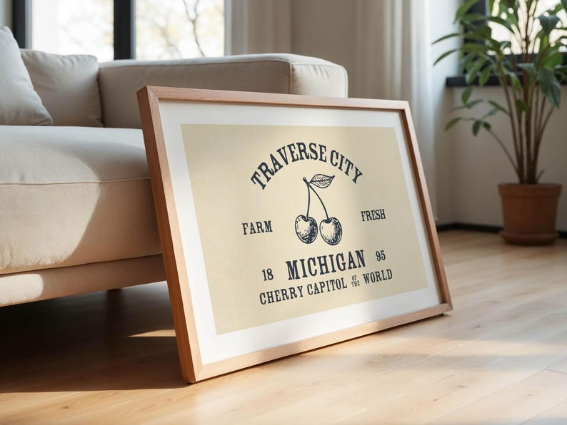 May include: Framed print with a light beige background and a wooden frame. The print features the words "Traverse City" above a cherry illustration. Below the cherries are the words "Farm", "Michigan", and "Cherry Capitol of the World".