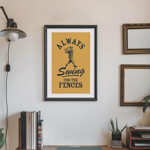 May include: Framed baseball-themed art print with a mustard-yellow background and black text that reads "Always Swing for the Fences." The artwork features a baseball player in silhouette.