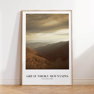 Op de afbeelding: Een ingelijste print van een landschapsfoto van het Great Smoky Mountains National Park. De afbeelding toont een mistige, goudkleurige bergketen met een bewolkte lucht.