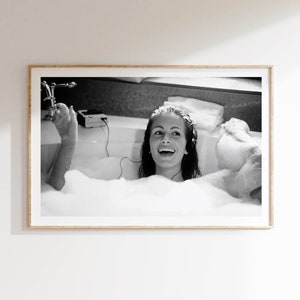 Peut inclure: Une photographie en noir et blanc d'une femme dans une baignoire remplie de bulles. Elle sourit et &eacute;coute de la musique avec des &eacute;couteurs.