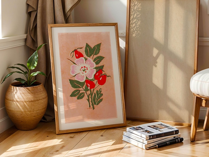 May include: A framed print of a pink and white rose with red berries on a light pink background. The frame is made of wood and has a natural finish.