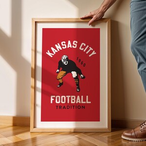 May include: A framed poster with a red background and white text that reads "Kansas City 1960 Football Tradition". A vintage illustration of a football player in a helmet and uniform is in the center of the poster.