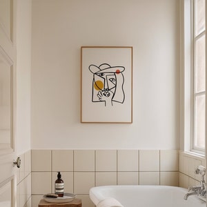 May include: A framed black and white line drawing of a person's face with a hat. The drawing is on a white background and has yellow and red circles.