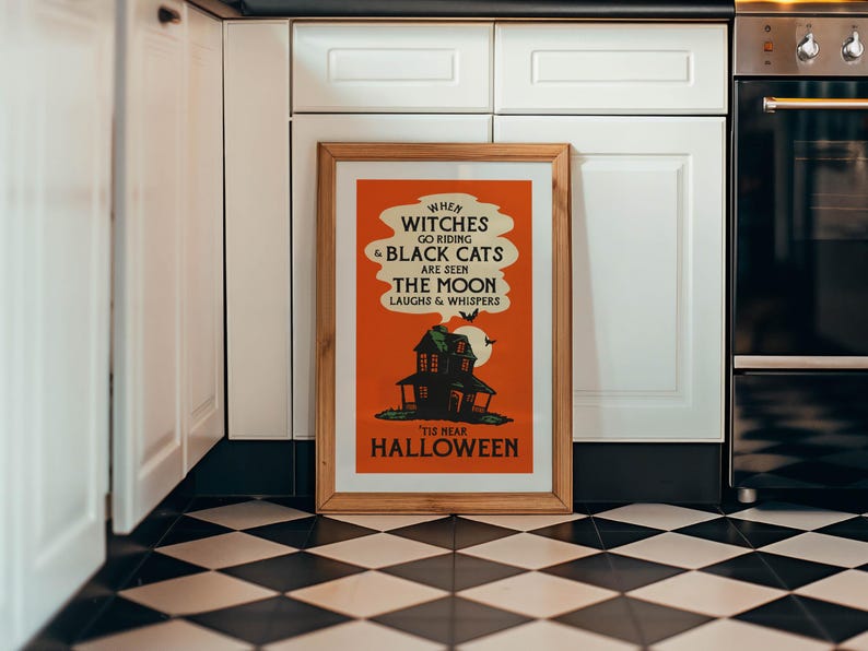 May include: A framed Halloween-themed poster with an orange background and a vintage design. The poster features a haunted house, bats, and the text "WHEN WITCHES GO RIDING & BLACK CATS ARE SEEN THE MOON LAUGHS & WHISPERS 'TIS NEAR HALLOWEEN".