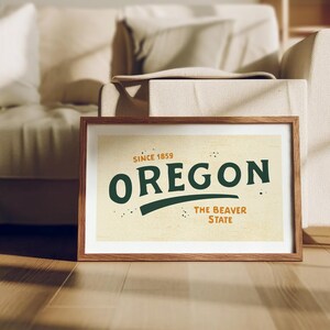 May include: A framed print with a vintage design featuring the text "Oregon, Since 1859, The Beaver State" in green and orange lettering on a beige background.