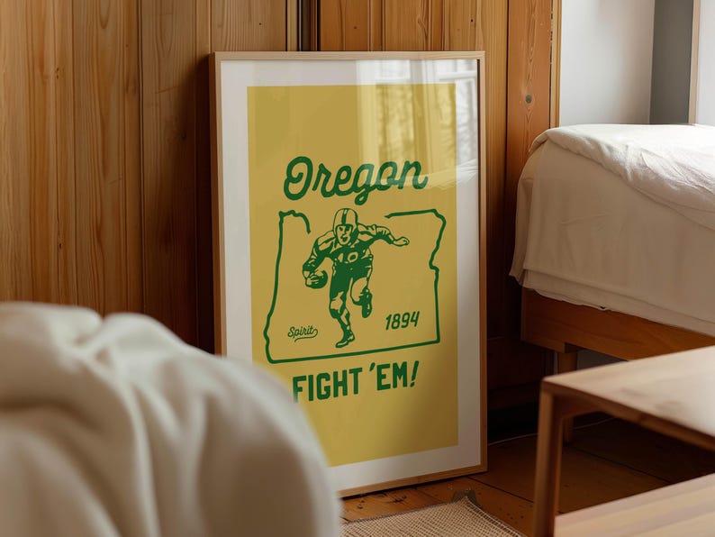 K&ouml;nnte beinhalten: Ein gerahmtes Poster mit gelbem Hintergrund und gr&uuml;nem Text und Grafiken. Das Poster zeigt "Oregon" &uuml;ber einer Footballspieler-Grafik und dem Text "Fight 'Em!". Das Jahr "1894" wird ebenfalls angezeigt.